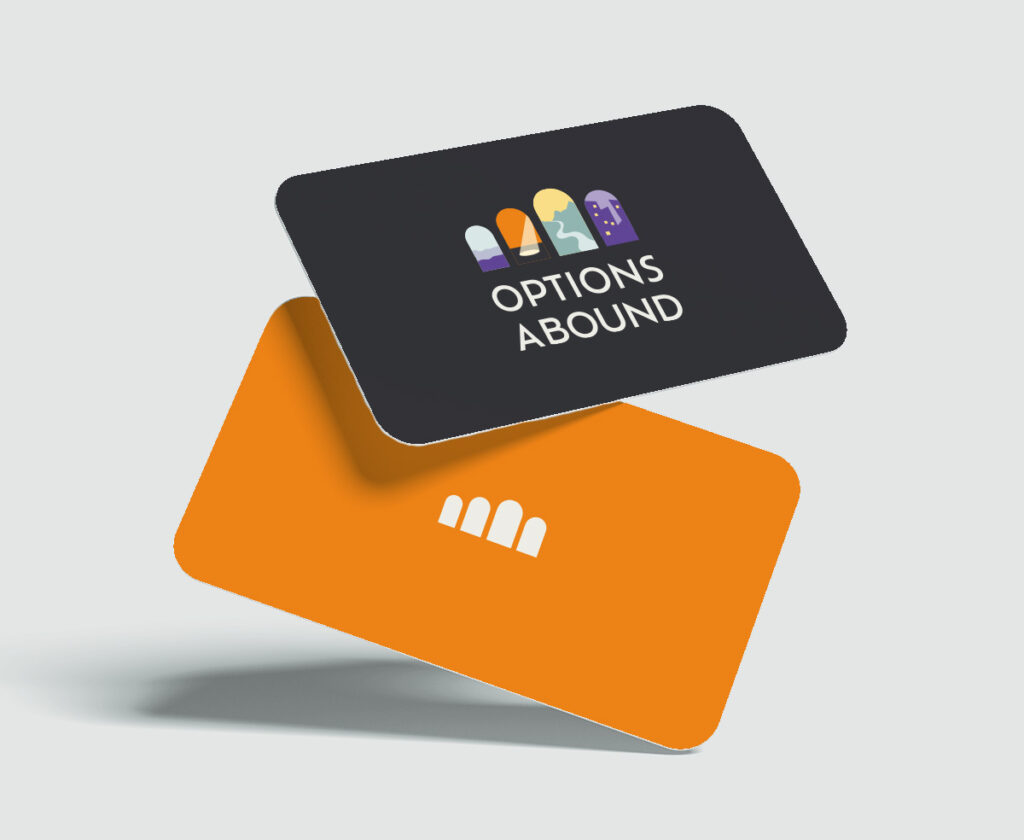Photos of two cards suspended in air. One is dark grey and displays the Options Abound logo with 4 arched doorways thru which we see illustrations different world scenes. The other card is orange with an icon of 4 arches.
